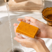 Turmeric and kojic cleansing bar lathered between adult hands